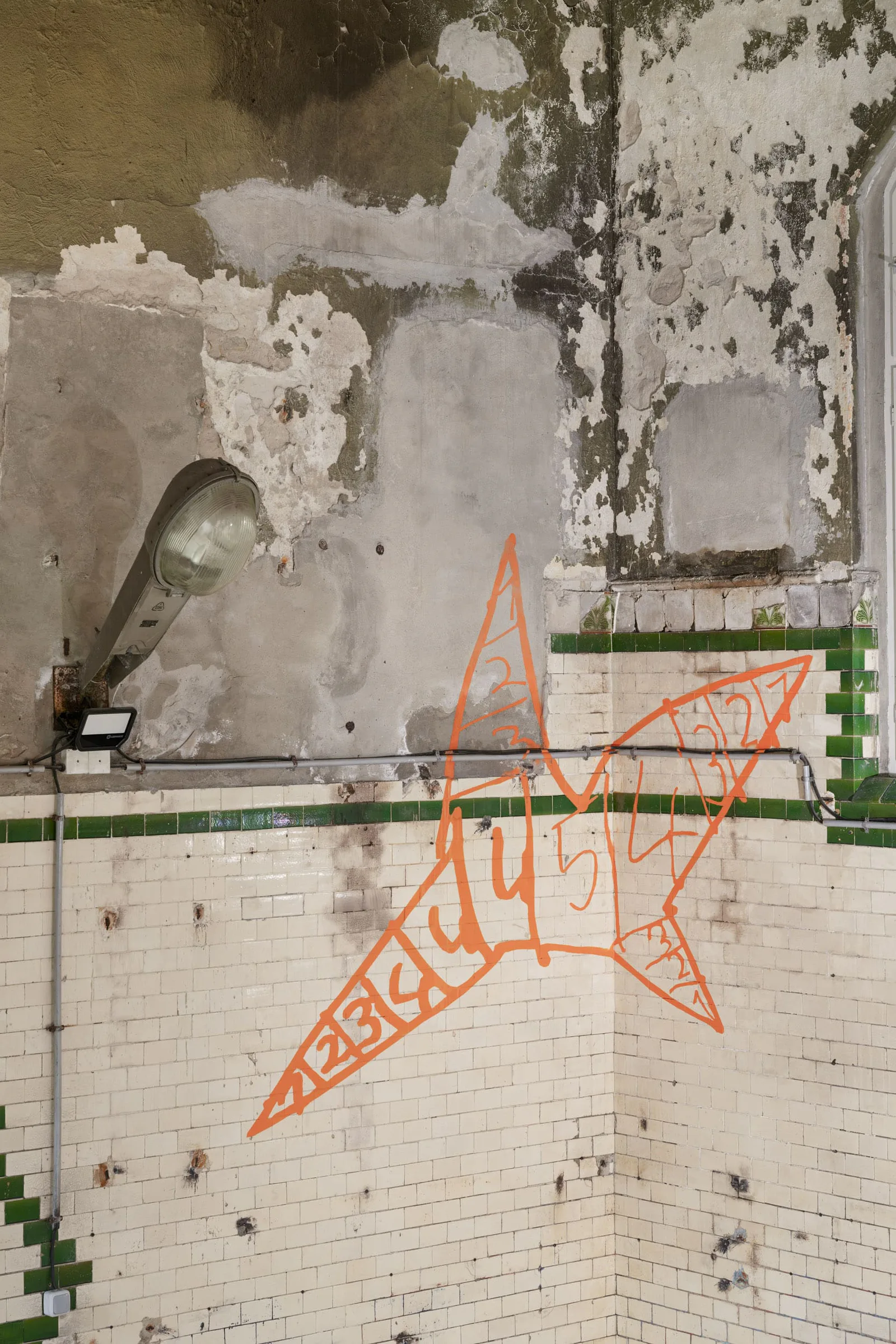 Neue Erinnerungen: orangefarbene Figur mit kyrillischer Schrift an einer verwitterten Kachelwand