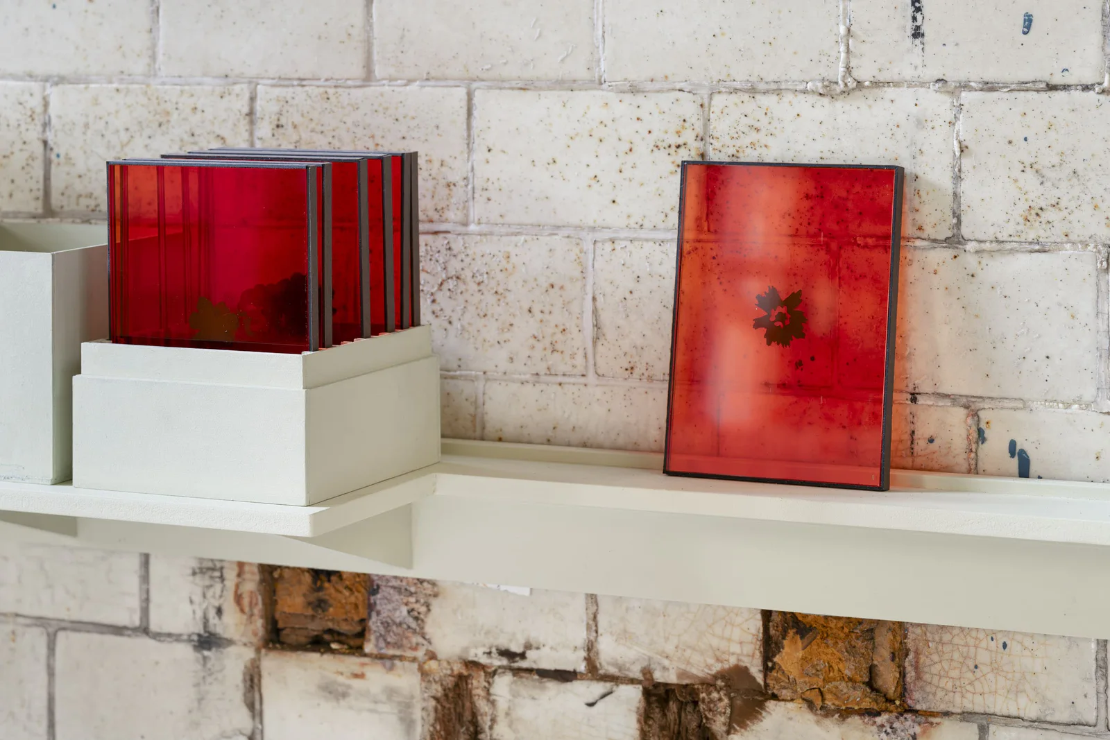 Neue Erinnerungen: rote Glasobjekte und ein roter Rahmen auf einem weißen Regalbrett vor einer Kachelwand