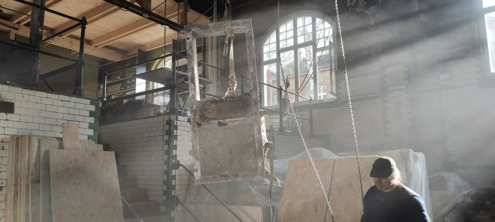 Bauarbeiten im neuen Ausstellungsort im Pumpwerk Berlin, Sonnenlicht fällt durch ein Fenster auf einen Arbeiter
