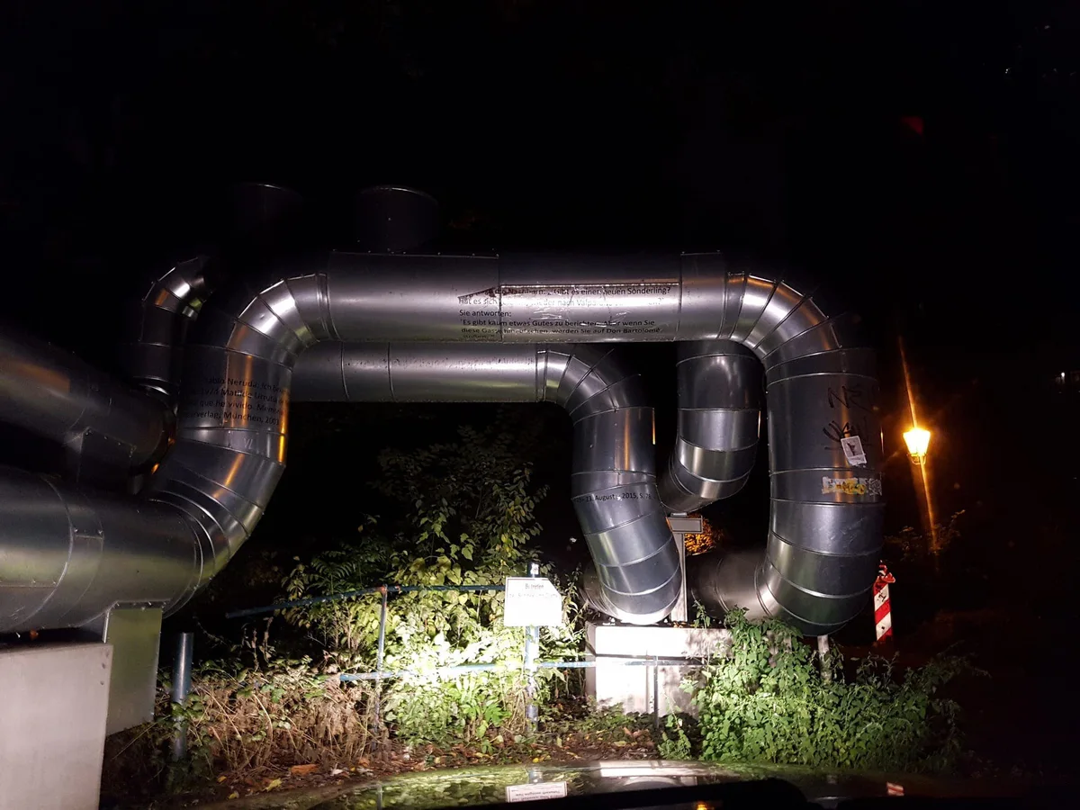 Night shot of silver pipes running in bends above a hedge