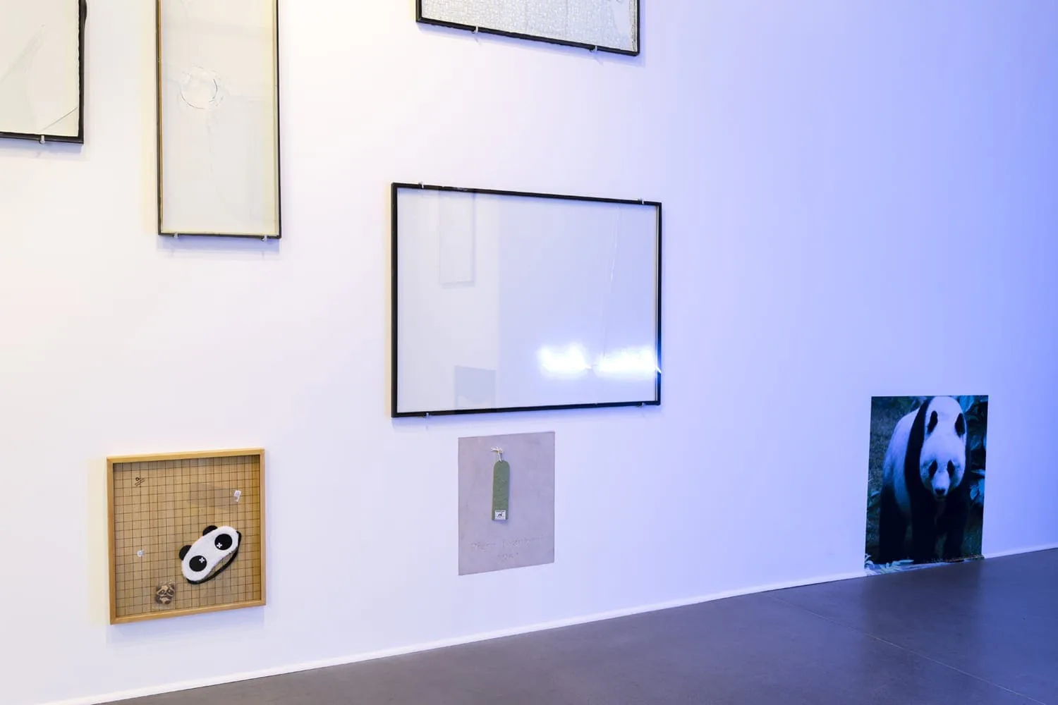 Installation view: empty frames and small pictures, including a panda motif, on a blue-lit wall