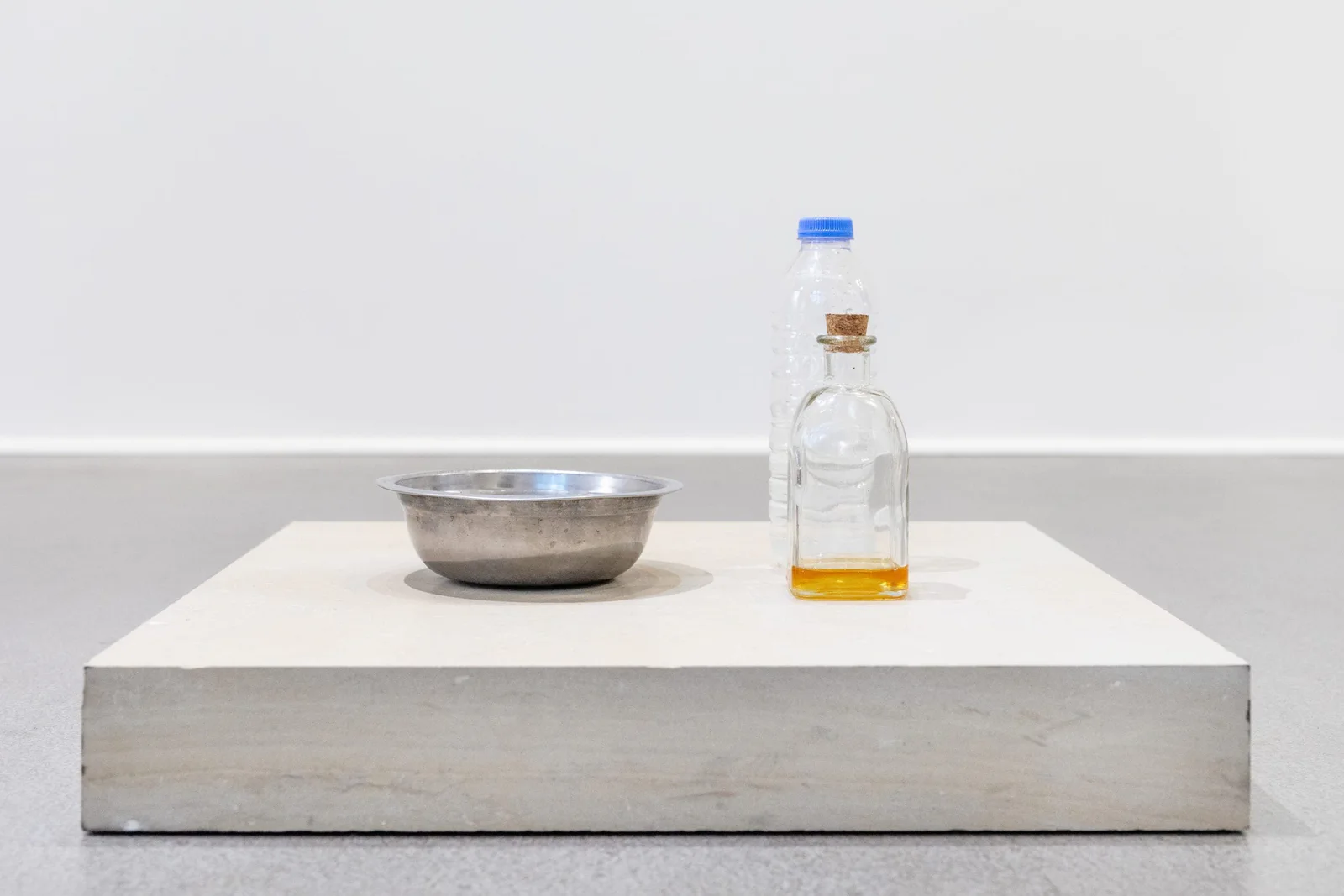 Installation view: a bowl and a bottle of honey on a flat white plinth