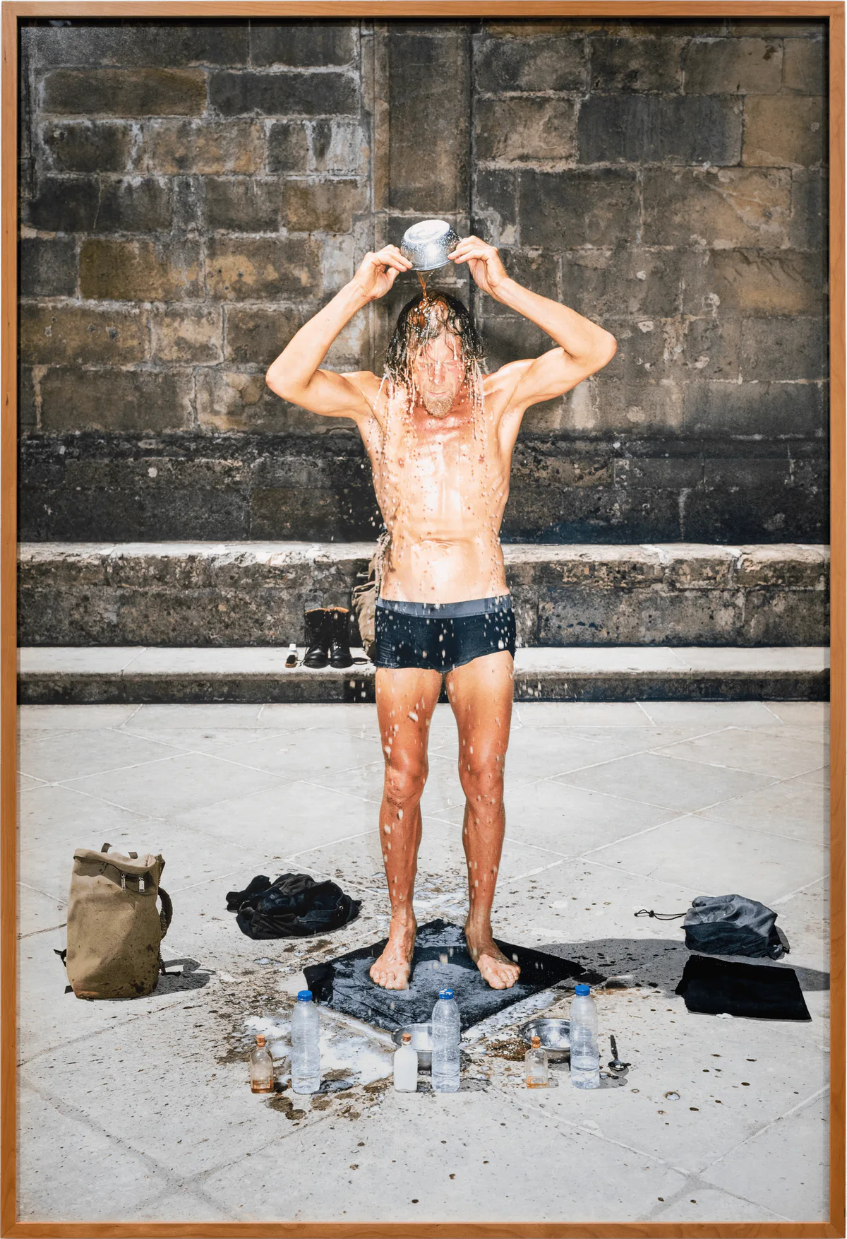 GABRIEL – MA I – Die Dritte Waschung oder die Honigtaufe, 2019: ein Mann in Badehose gießt sich vor einer Steinmauer Wasser über den Kopf
