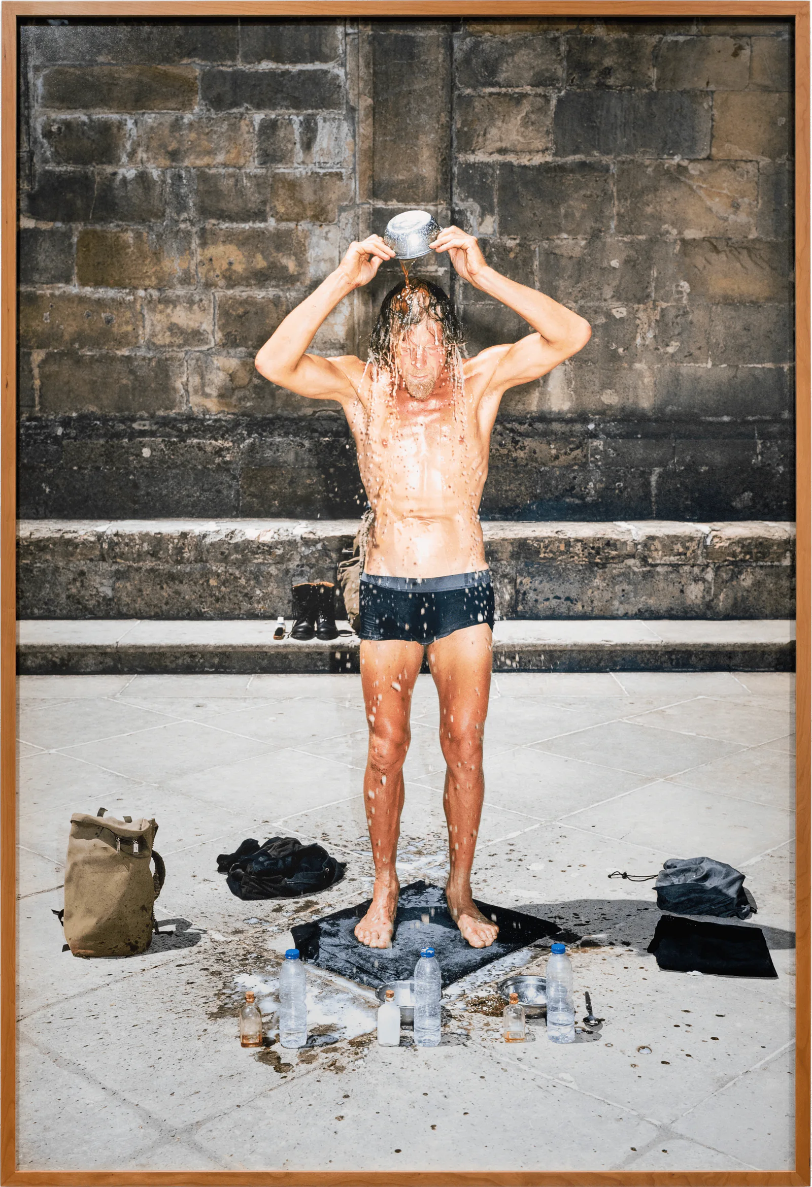 GABRIEL – MA I – Die Dritte Waschung oder die Honigtaufe, 2019: ein Mann in Badehose gießt sich vor einer Steinmauer Wasser über den Kopf