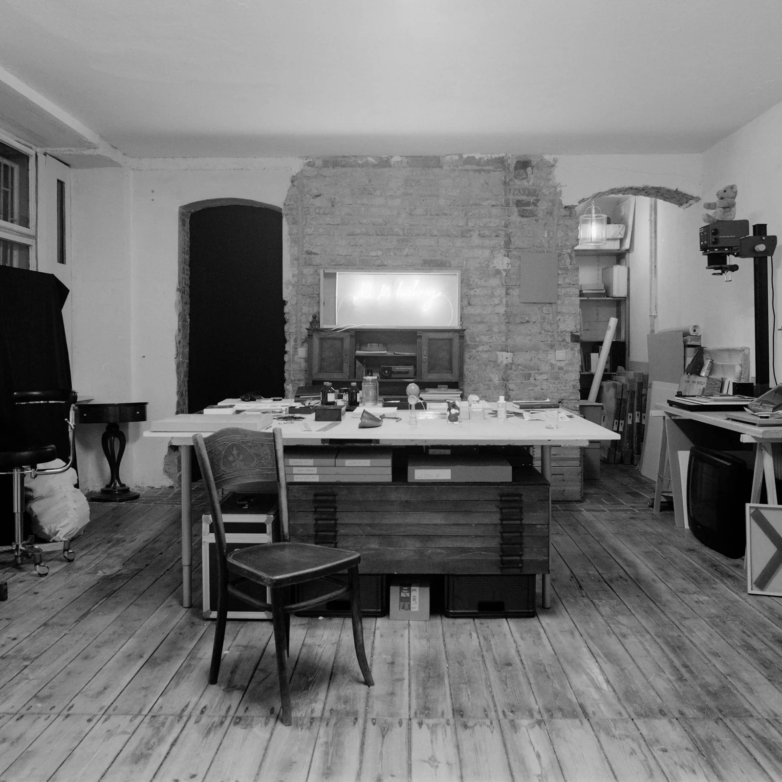 Max Schwarzmann: studio with a large worktable, chairs and pictures on a brick wall, black and white