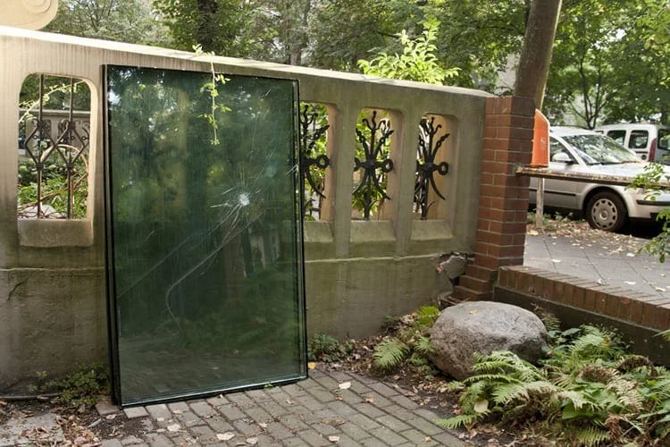 Large pane of glass leaning against a garden wall with a railing, a street with cars behind