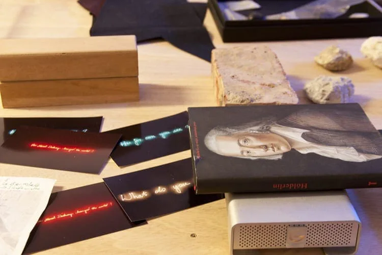 Table with a small framed portrait, black panels with red and blue lettering lights, stones and wooden boxes