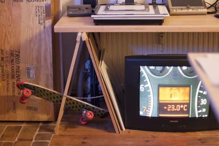 A tube television showing a car dashboard with speedometer and temperature readout, beside a skateboard and a wooden crate