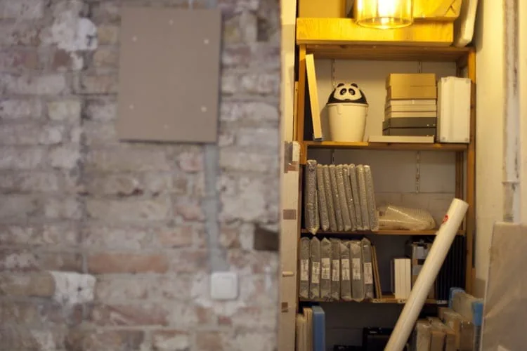 Lit shelf in a niche of a brick wall with books, boxes and a small figure