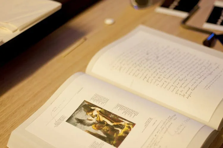 Open book on a table showing a small colour illustration of a Renaissance scene