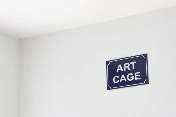 Michal Martychowiec, Art Cage: blaues Emailleschild mit der Aufschrift „ART CAGE“ in einer weißen Raumecke