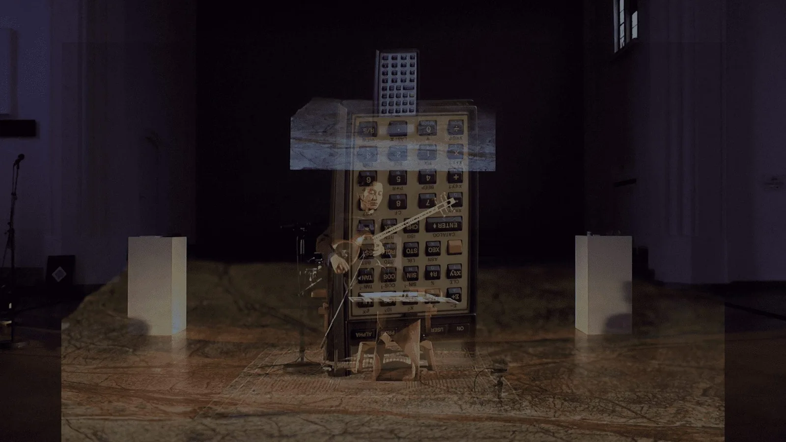 Elies Miniatures, Performance: eine Projektion über einem Objekt in einem abgedunkelten Raum, davor Zuschauer
