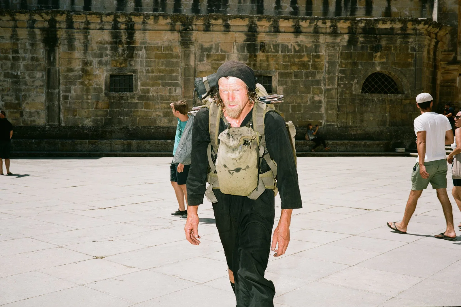 GABRIEL, Der Soldat, der keinen Krieg führen sollte: Mann mit Mütze und großem Rucksack auf einem Platz vor einer Klostermauer