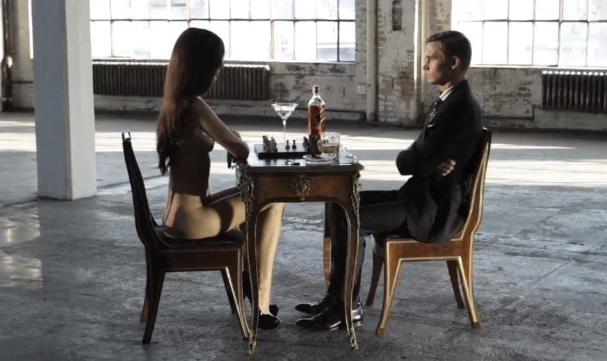Gavin Bond: a naked woman and a man in a suit sitting opposite each other at a chess table in an empty factory hall