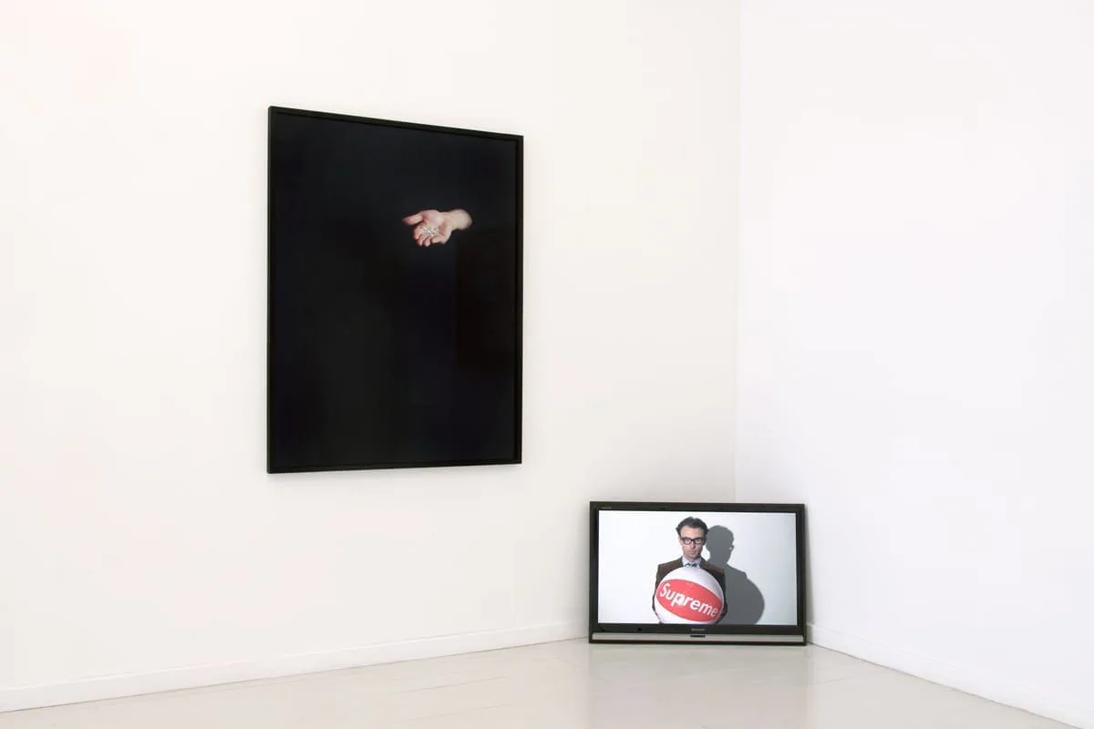 What remains the poets provide, installation view: black picture with an open hand on the wall, a framed picture on the floor