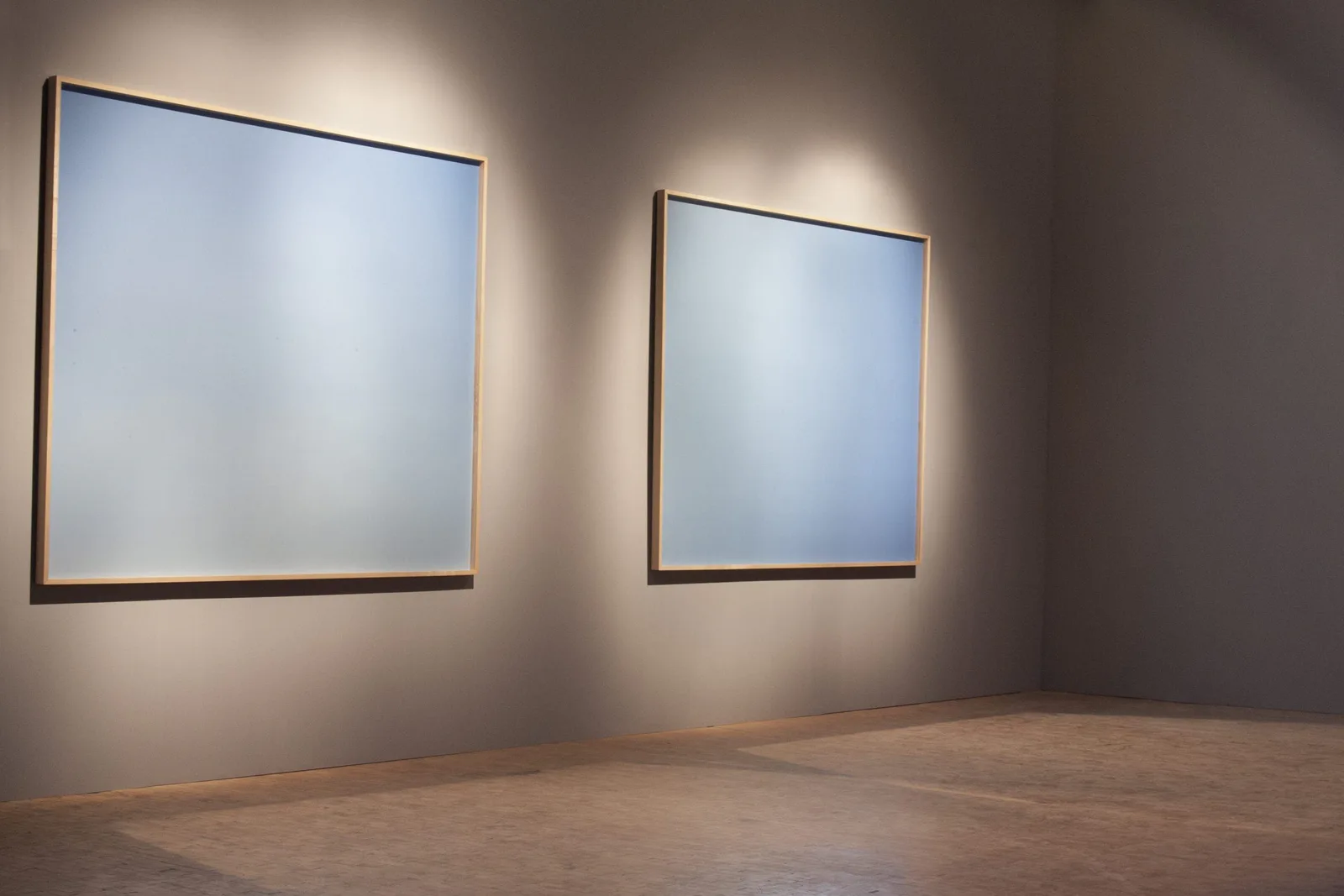 Installation view: two large pale blue pictures on a wall under spotlights