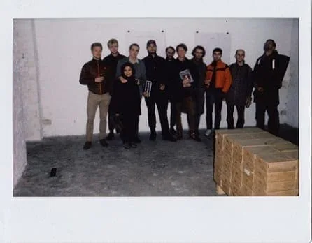 Max Schaffer – In Erwartung des Kommenden Gottes: Polaroid of a group of people behind stacked wooden crates in a gallery room