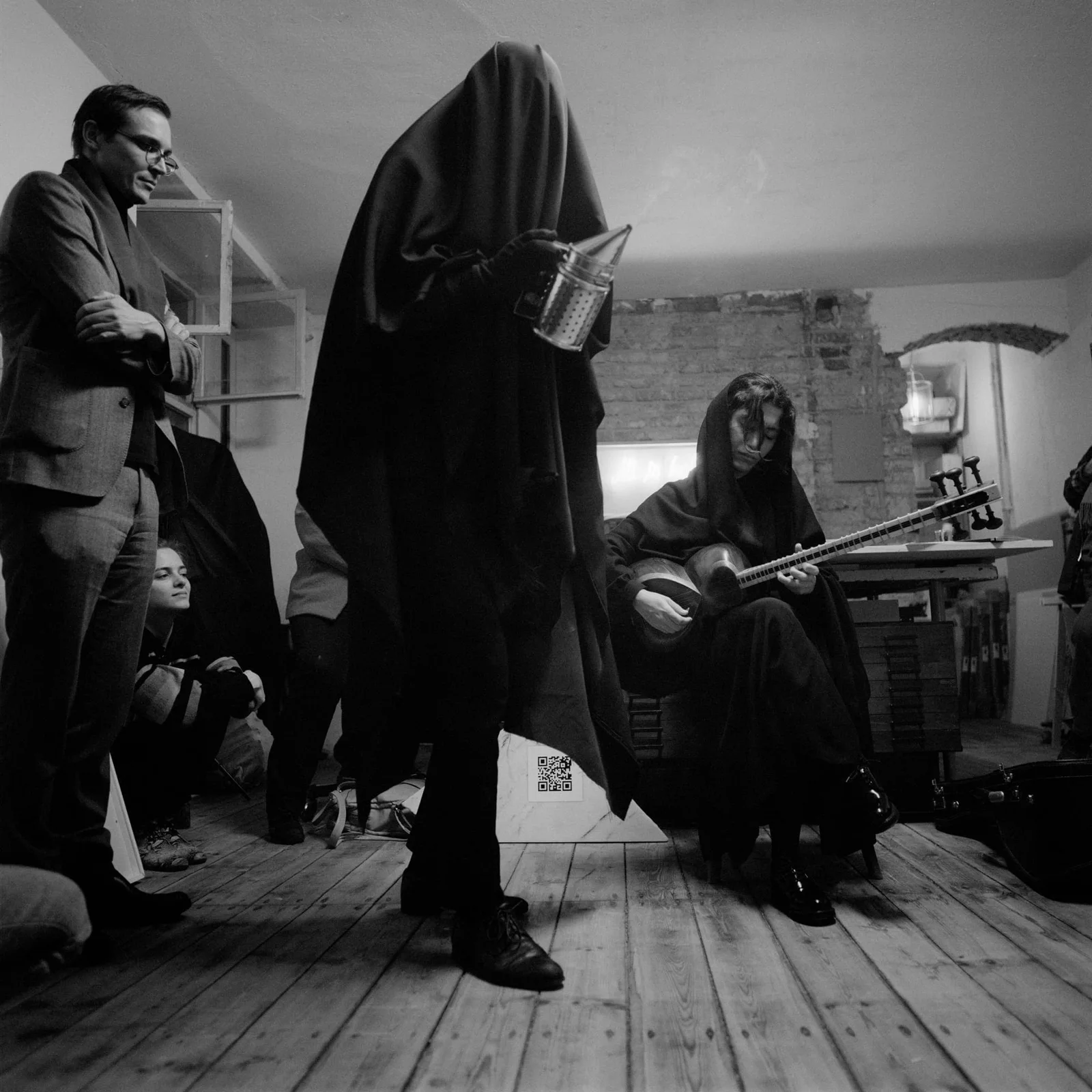 Max Schwarzmann: a figure veiled entirely in black standing among spectators, Elshan Ghasimi seated beside with her tar, black and white