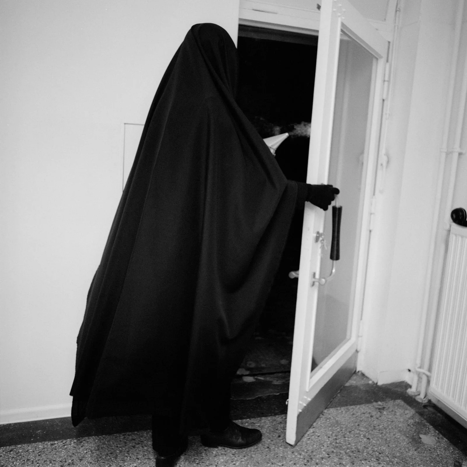 Max Schwarzmann: a figure veiled in black stepping through an open door, black and white