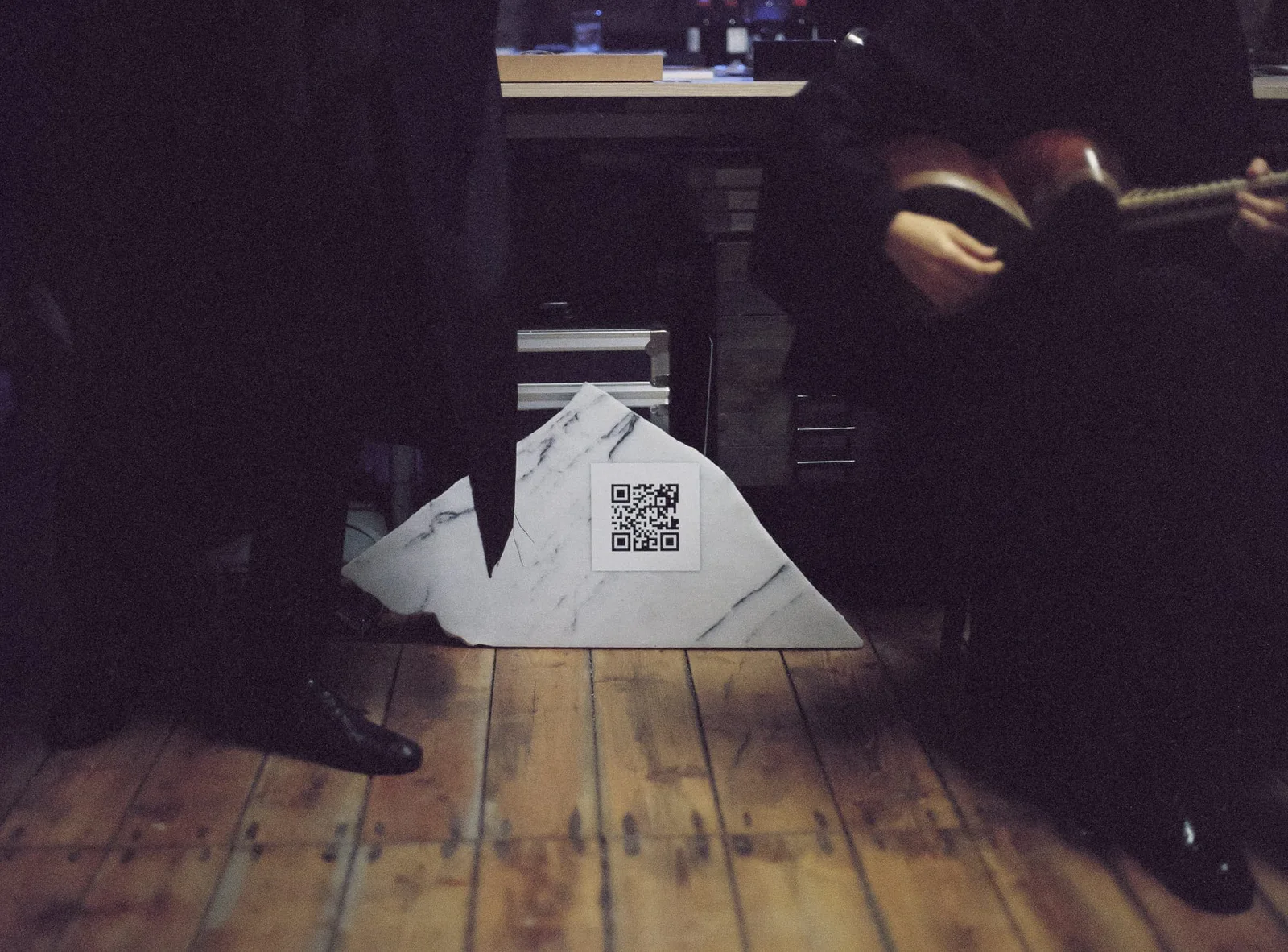 Stefan Hähnel – The Coming God: a piece of marble with a QR code on wooden floorboards, behind it Elshan Ghasimi with her tar