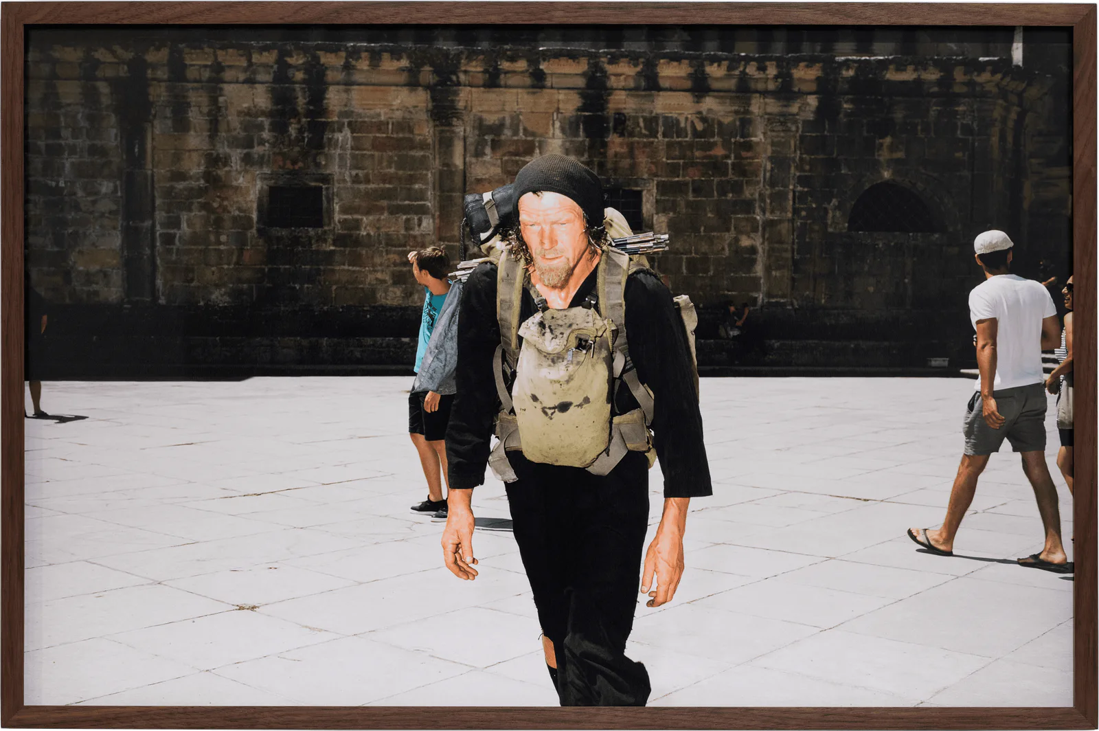 GABRIEL – Der Soldat der keinen Krieg führen wollte, 2019: framed photograph of a man with a backpack and hat on a square in front of a stone façade
