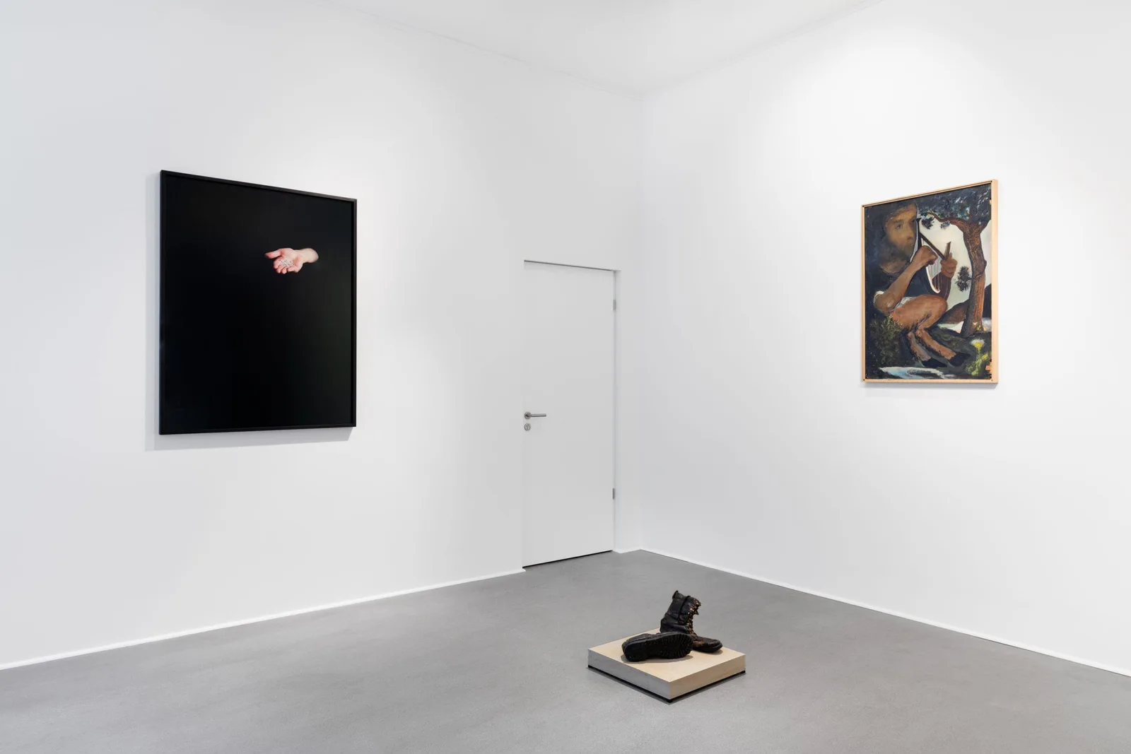 Exhibition view: white room with two paintings, a door and an object on the floor