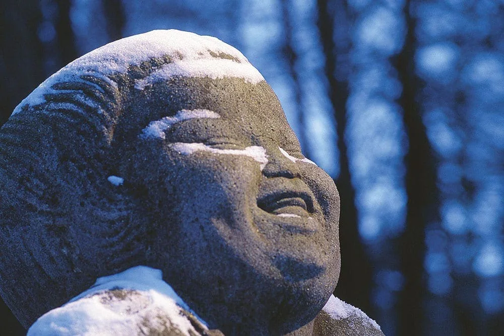 Bernhard Hoetgers Großplastik „Bonze des Humors“ (1914) in Worpswede, ein lachender Steinkopf mit Schnee bedeckt vor blauen Bäumen