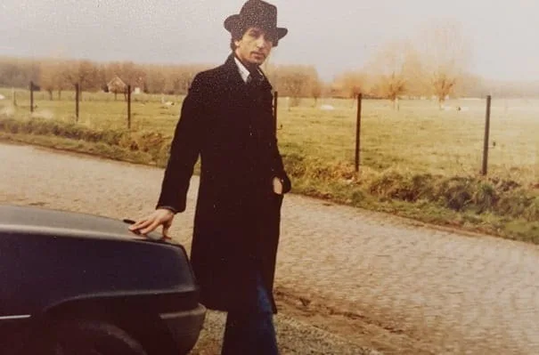 El Arbi Bouqdib als junger Mann mit Hut und dunklem Mantel neben einem Auto auf einer Landstraße