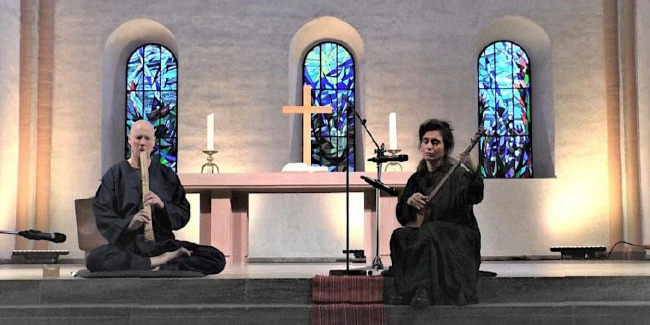 Elshan Ghasimi mit ihrer Tar und ein Musiker mit Shakuhachi vor dem Altar einer Kirche mit bunten Glasfenstern
