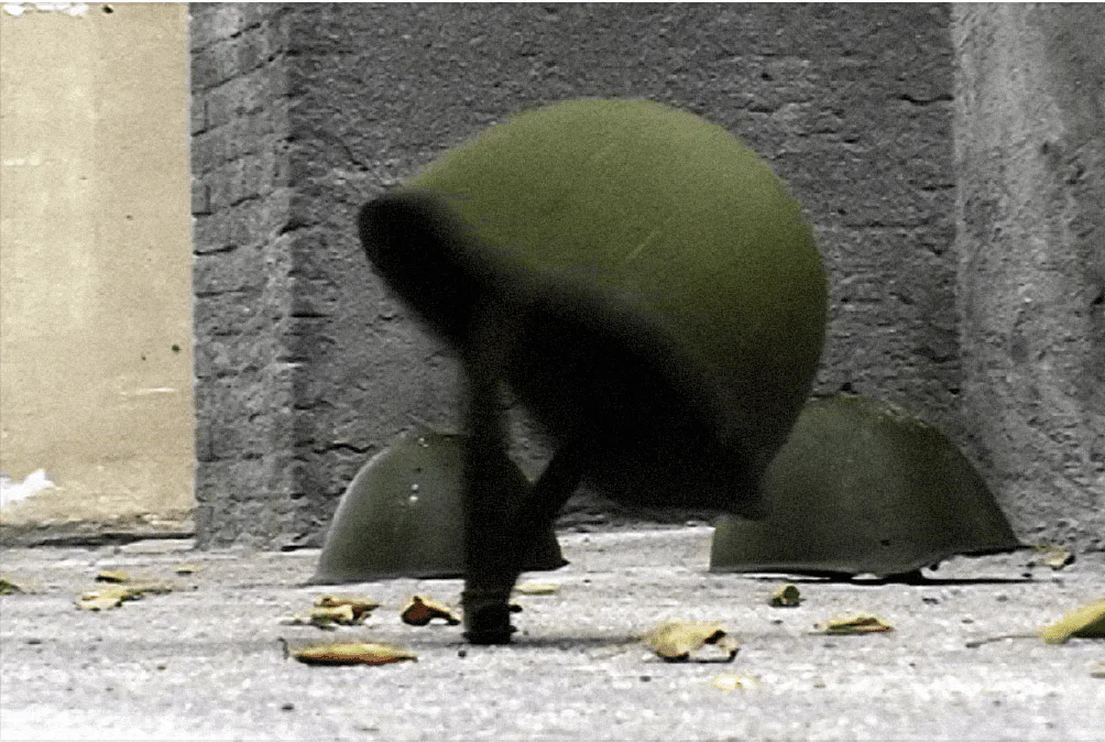 Sergey Bratkov, Endless War, Videostill, 2010: zwei grüne Stahlhelme auf einem Betonboden vor einer Mauer