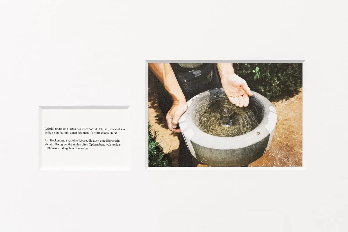 Marianische Wochen: gerahmtes Foto zweier Hände mit einem steinernen Wasserbecken neben einem Textblatt an der Wand