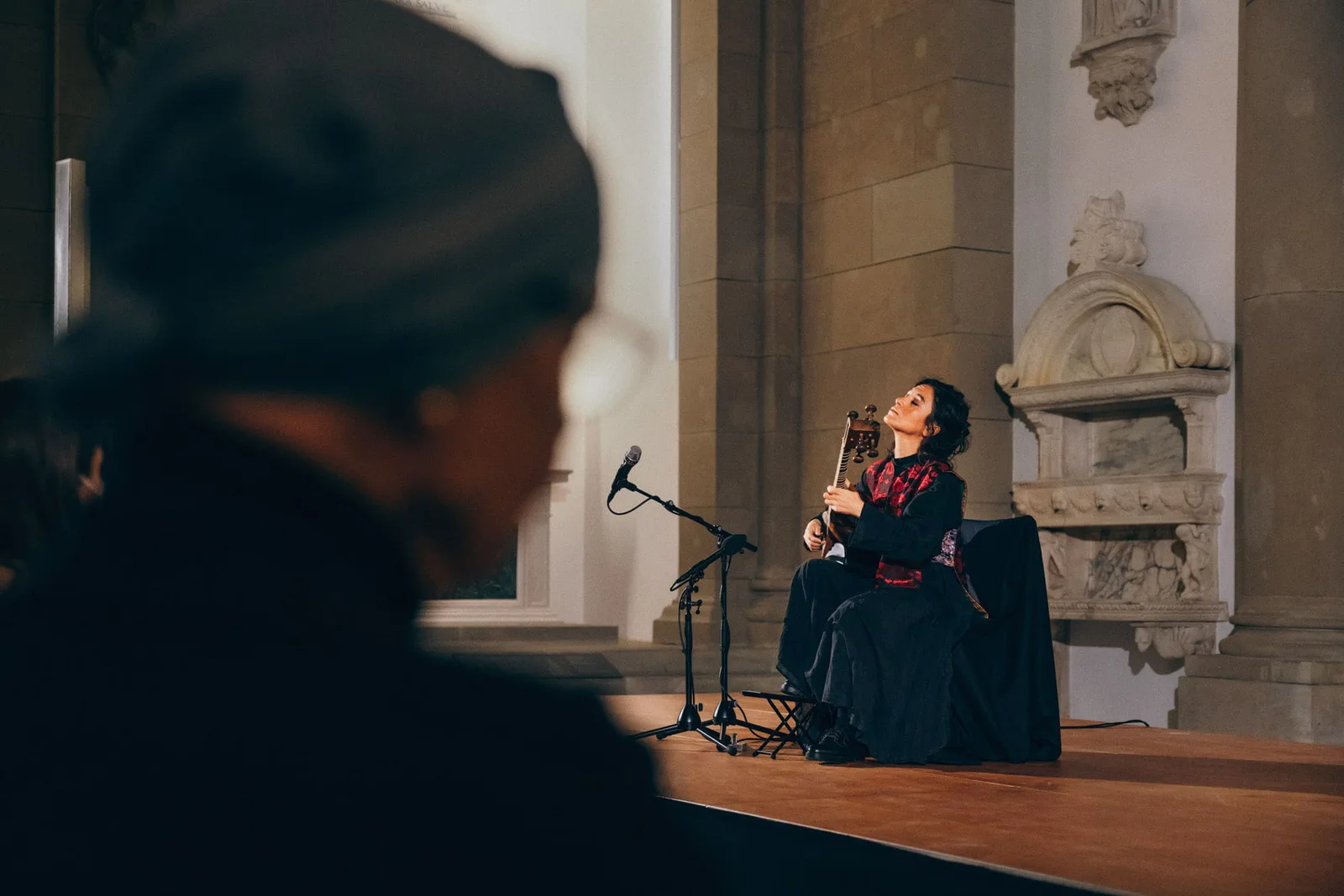 Elshan Ghasimi performing on stage in the basilica of the Bode-Museum, a blurred listener in a cap in the foreground