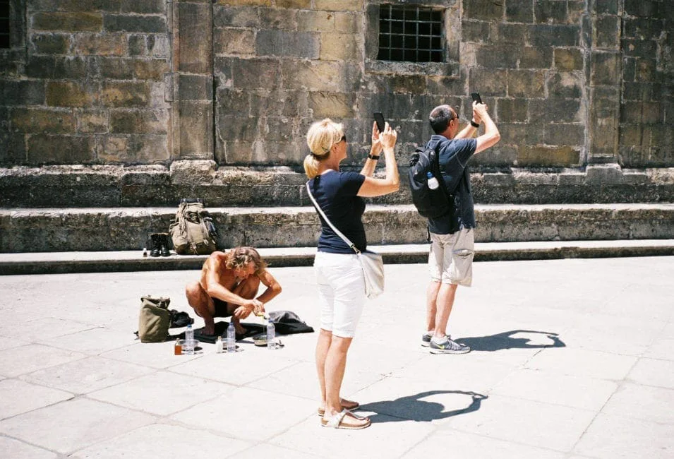 GABRIEL: a man kneeling in front of a church wall while two tourists photograph him