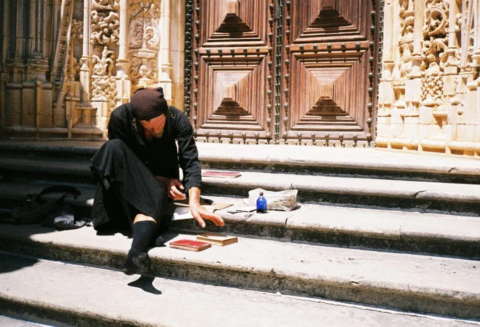 GABRIEL: a man in black sitting on the steps in front of a richly ornamented church portal