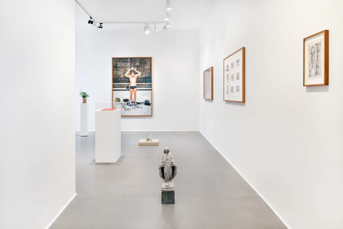 Marianische Antiphonen I, exhibition view: a photograph of a man in a garden, small sheets, a plinth with a figure and an object on the floor