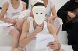 Symposion und Eranos: Personen in weißen Gewändern mit weißen Masken sitzen mit Papieren in den Händen