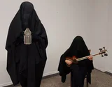 The Coming God: zwei ganz in Schwarz verhüllte Figuren, eine mit Laterne, die andere mit einer Tar