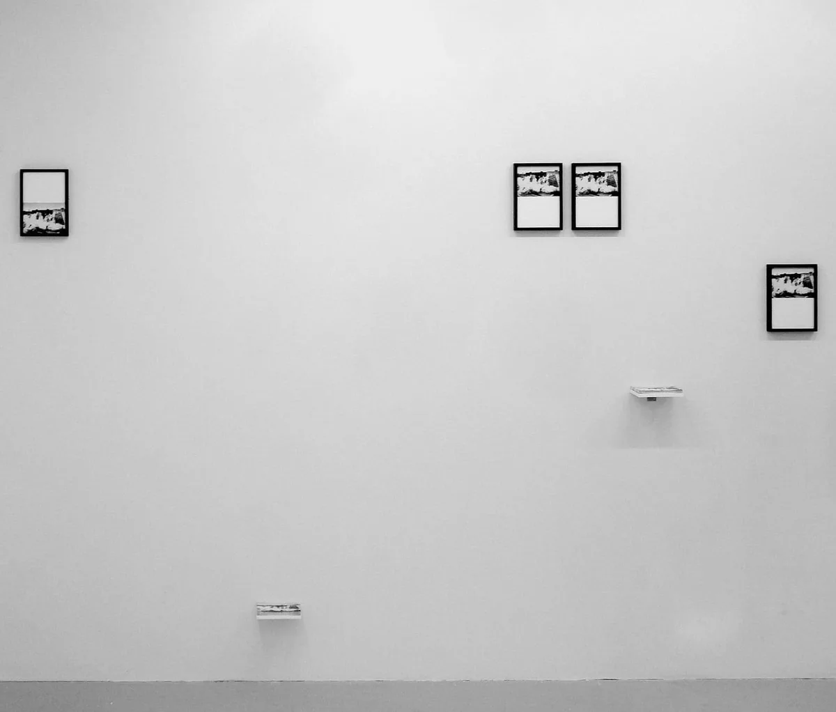 The road leads back and back to the black square: kleine gerahmte Fotografien verteilt an einer hohen weißen Wand