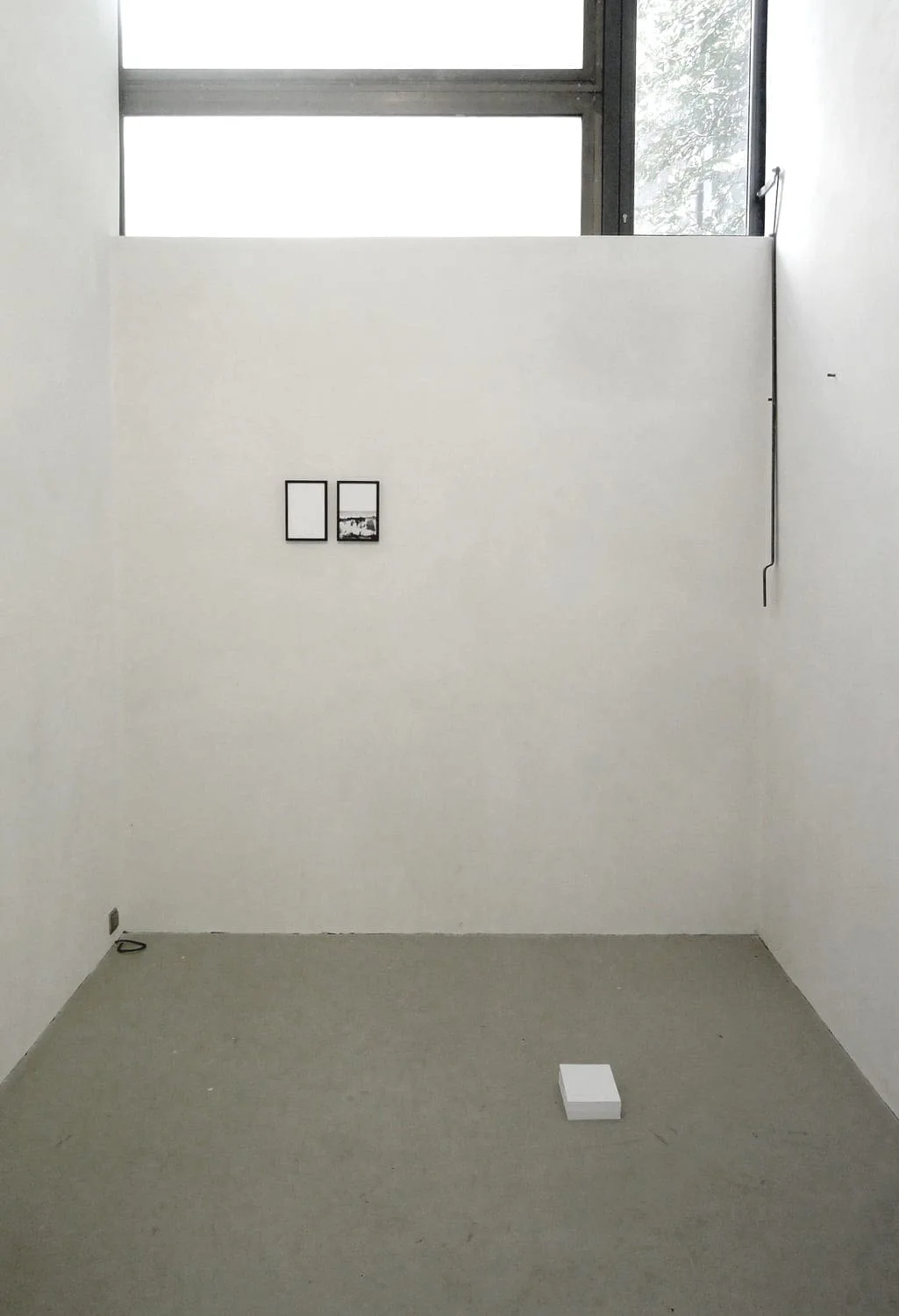 The road leads back and back to the black square: zwei kleine Rahmen an der Wand eines leeren Raums mit Fenster und einem Objekt am Boden