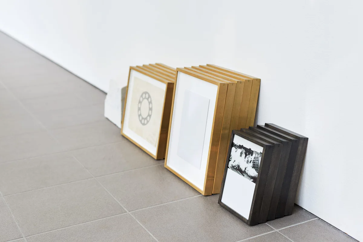 The road leads back and back to the black square: gerahmte Blätter und Fotografien, an eine Wand gelehnt auf grauem Boden