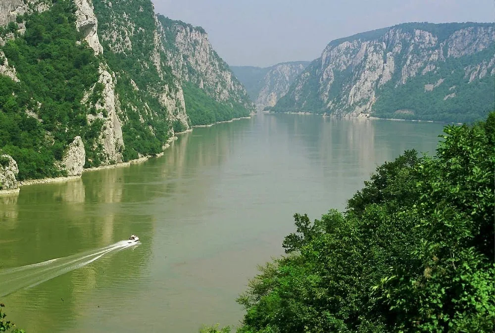 Die Donau am Eisernen Tor zwischen bewaldeten Felsufern, ein Boot auf dem Wasser